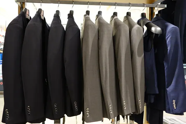 Charcoal, gray and navy suit jackets hanging in a row on a metal rack in a menswear clothing store