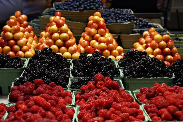 Farmers market stall with green baskets of raspberries, blackberries, blueberries and stacked yellow-red cherries