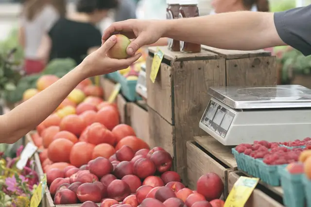 Hands passing fruit at a market stall with a weighing scale