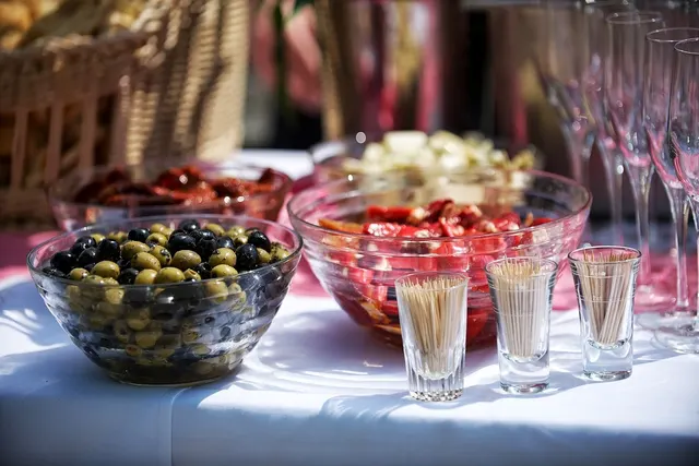 Outdoor catering table with bowls of olives, sun-dried tomatoes and cheese, toothpick cups and champagne flutes