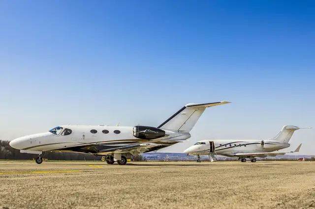 Two small private jets parked on an airfield under blue sky