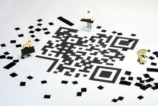 Miniature worker figurines assembling a large black-and-white QR code from scattered square pieces on a white surface