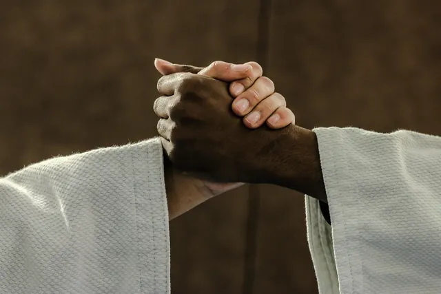 Close-up of two martial artists in white judo gis clasping hands in a firm grip against a dark dojo wall