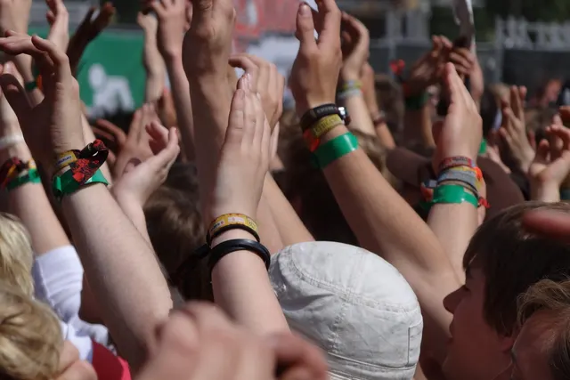 Festival crowd raising their hands, wrists stacked with colorful fabric event wristbands on a sunny day