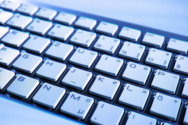 Close-up of a silver computer keyboard with white keys in a German QWERTZ layout, lit with a cool blue tint