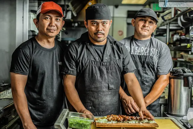 Three chefs in aprons standing at a kitchen prep counter