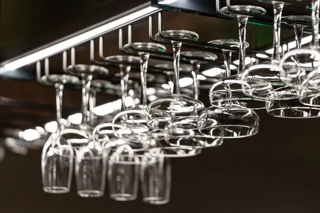 Rows of clean wine glasses hanging upside down from an overhead metal rack above a restaurant bar