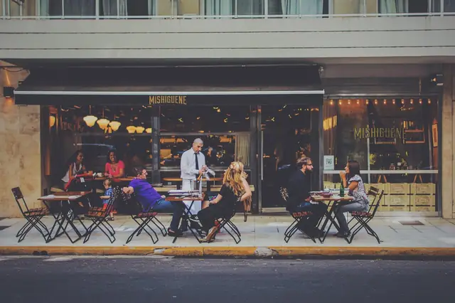 Diners at outdoor sidewalk tables in front of a restaurant