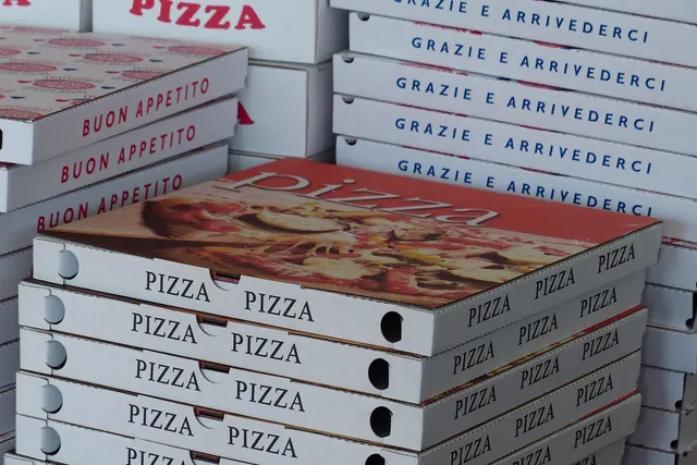 Stacks of white takeout pizza boxes printed with PIZZA, Buon Appetito and Grazie e Arrivederci, ready for to-go orders