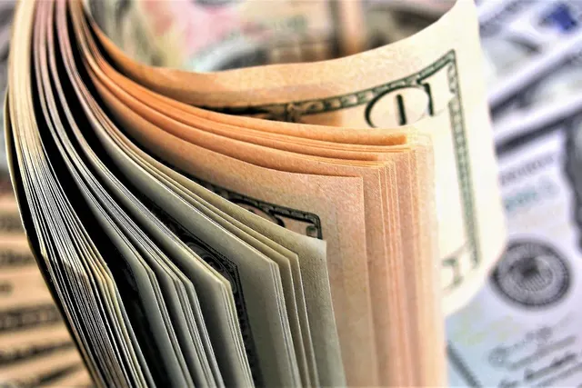 Close-up of a fanned stack of US dollar bills curled upright in front of blurred $100 banknotes