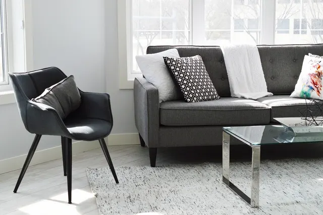 Bright living room with a gray tufted sofa, black accent chair, glass coffee table and patterned throw pillows