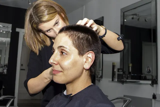 Hairstylist checks a woman's freshly cropped short haircut while she sits caped in a salon chair by mirrors