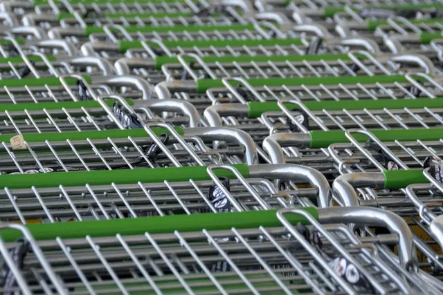 Rows of nested metal grocery shopping carts with green handles lined up close together at a supermarket