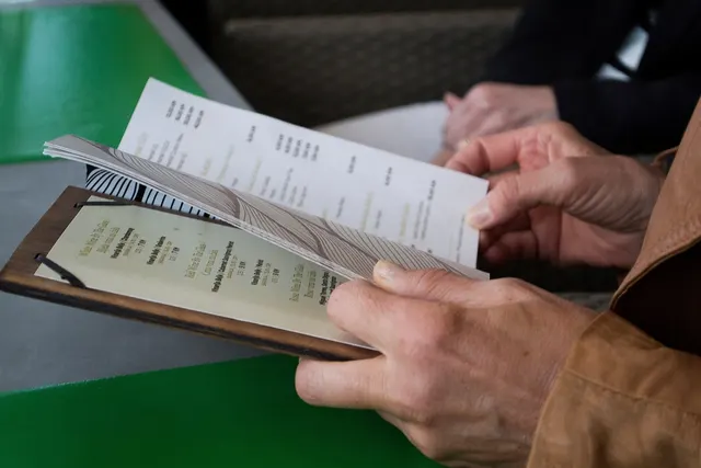 Close-up of a diner's hands holding a paper menu on a wooden clipboard at a restaurant table
