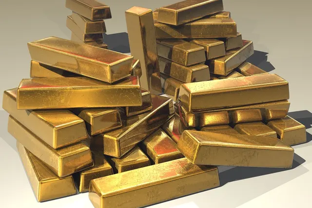 Pile of shiny gold bullion bars stacked haphazardly on a light gray surface