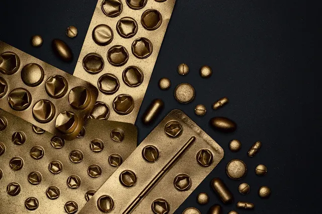 Gold-colored blister packs and scattered tablets and capsules on a black background