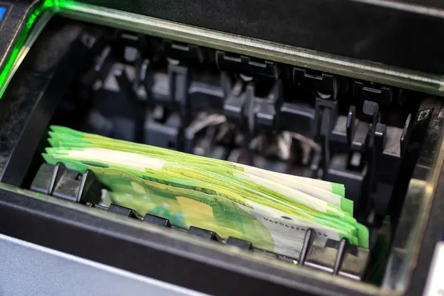 Stack of green 100 euro banknotes loaded in the tray of a black cash counting machine