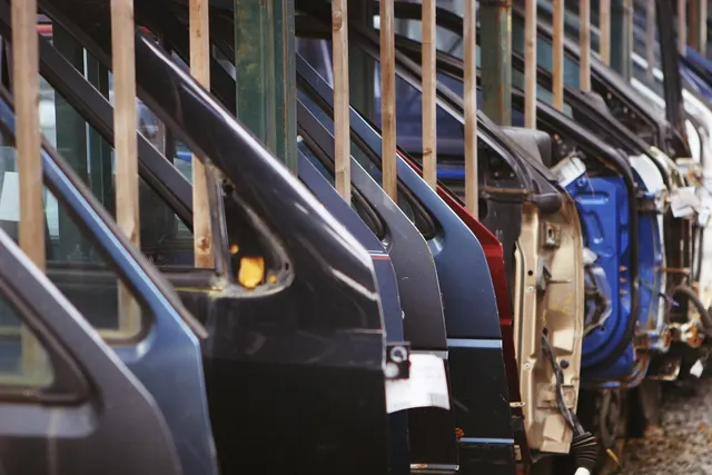 Row of car doors in black, blue, red and primer finishes stored upright in a rack at an auto parts facility