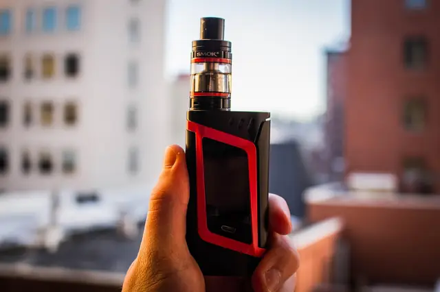 Hand holding a black and red vape mod outdoors