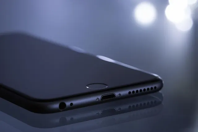 Close-up of a black smartphone's bottom edge and home button on a reflective surface with soft bokeh lights