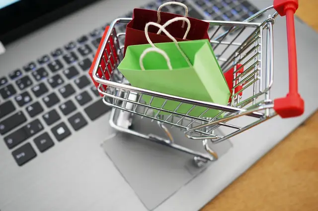 Miniature shopping cart with colorful bags on a laptop keyboard