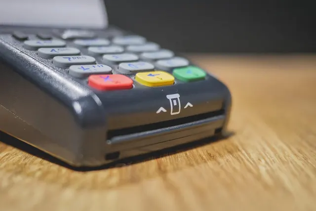 Close-up of a dark gray card payment terminal with chip card slot and red, yellow and green keys on a wooden counter