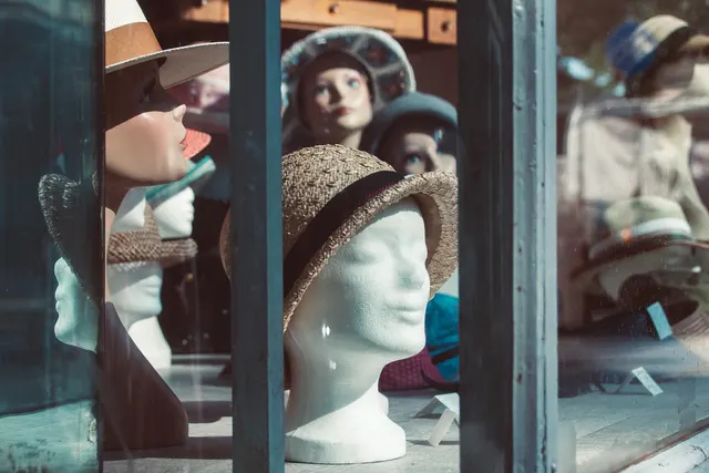 Boutique shop window displaying straw and felt hats on white foam and painted mannequin heads behind glass panes