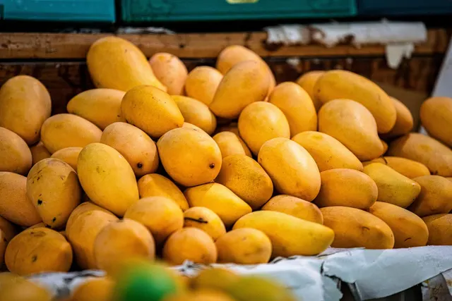 Pile of ripe yellow mangoes stacked on a wooden fruit stall at an outdoor market