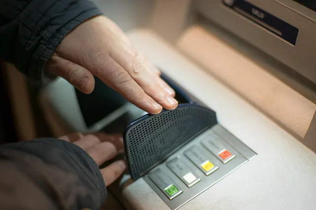 Person shielding an ATM keypad with one hand while entering a PIN with the other