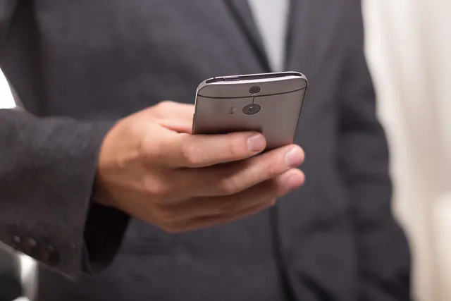 Close-up of a businessman in a dark gray suit holding a silver smartphone in one hand