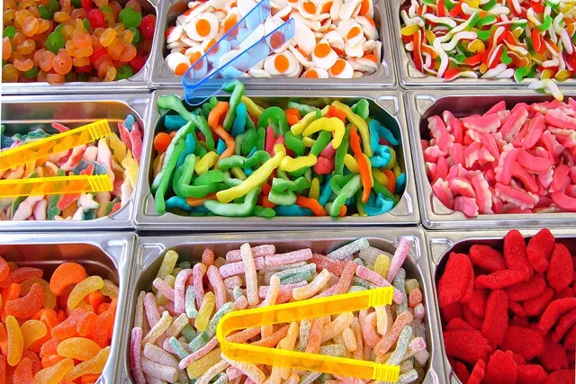 Self-serve bins of colorful gummy candy, including sour worms, fried-egg gummies and sugar-coated sticks, with plastic tongs