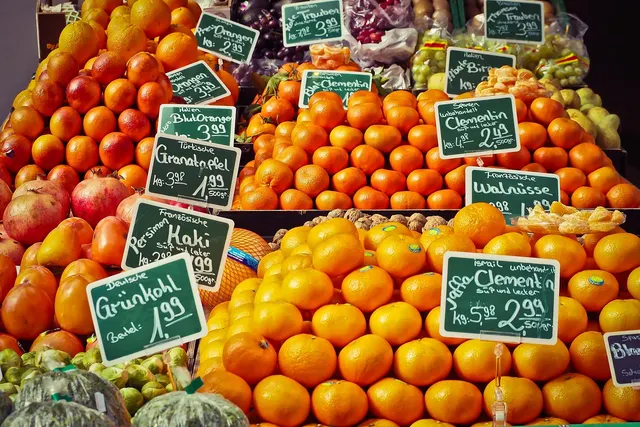 Grocery produce display of oranges, clementines, pomegranates and persimmons with handwritten chalkboard price signs
