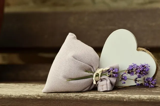 Linen lavender sachet tied with twine beside a white wooden heart and fresh lavender sprigs on a weathered bench