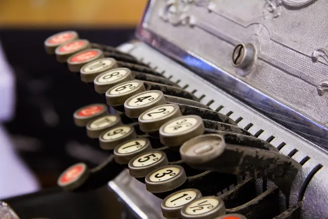 Close-up of worn round number keys on an antique metal cash register, including red-topped keys and fractions
