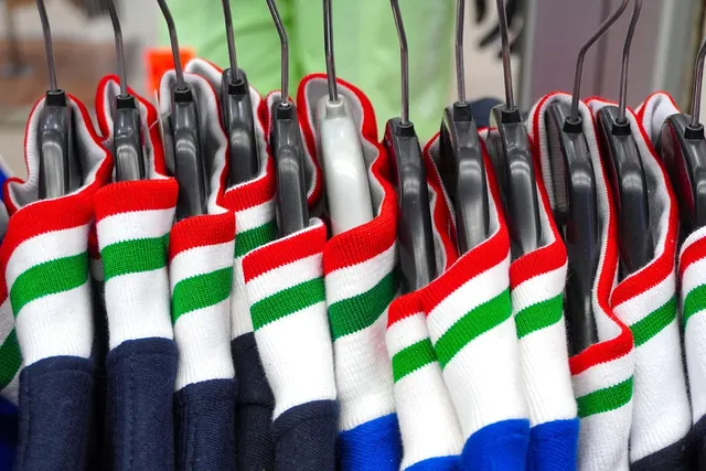 Row of navy shirts with red, white and green striped collars hanging on black hangers on a boutique clothing rack