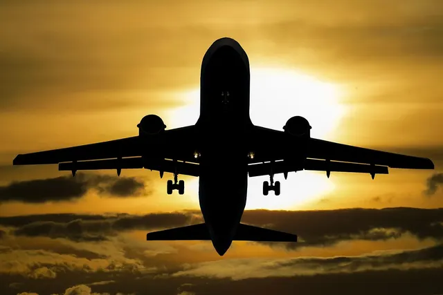 Silhouette of a twin-engine jet airliner taking off, landing gear down, against a golden sunset sky with clouds