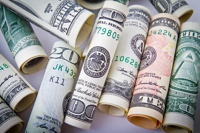 Rolled US dollar bills in 20, 10, 2 and 100 denominations scattered on a light surface