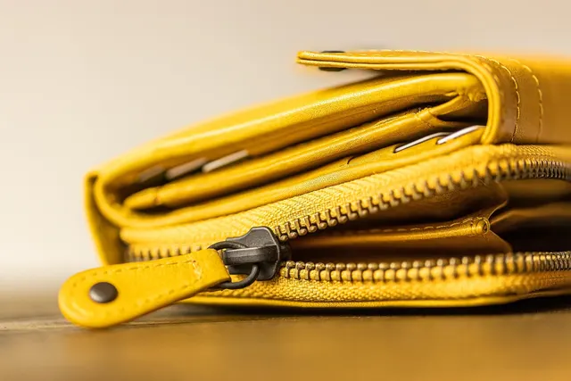 Close-up of a yellow leather zip wallet lying on a wooden table, with card edges visible in its slots