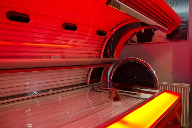 Open tanning bed glowing with red light inside a salon room, with a towel resting on the acrylic bed surface