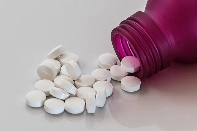 White round tablets spilling from a tipped-over magenta pill bottle onto a glossy light gray surface