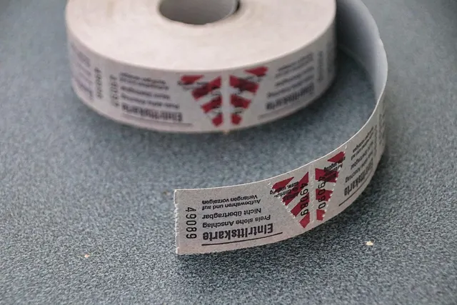 Roll of numbered paper admission tickets with red triangle print, one ticket unrolled on a gray countertop