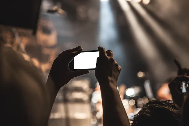 Concertgoer holds up a smartphone with a blank white screen to record a live show under bright stage lights
