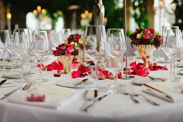 Elegant banquet table with white tablecloth, wine glasses, silverware, and pink rose centerpieces in gold vases