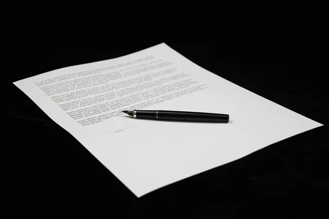 Printed document with a blank signature line and a black fountain pen resting on it against a black background