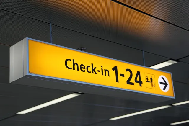 Yellow airport sign reading Check-in 1-24 with an arrow, hanging from a dark terminal ceiling with strip lights