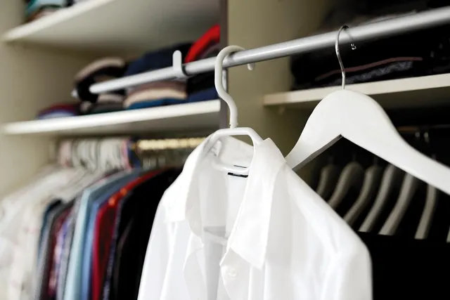 White dress shirt on a white hanger in a closet, with rows of colorful shirts and folded sweaters on shelves behind