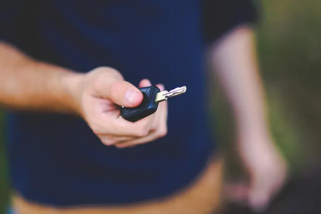 Man in a navy t-shirt holding out a car key with a black remote fob, as if handing over a vehicle