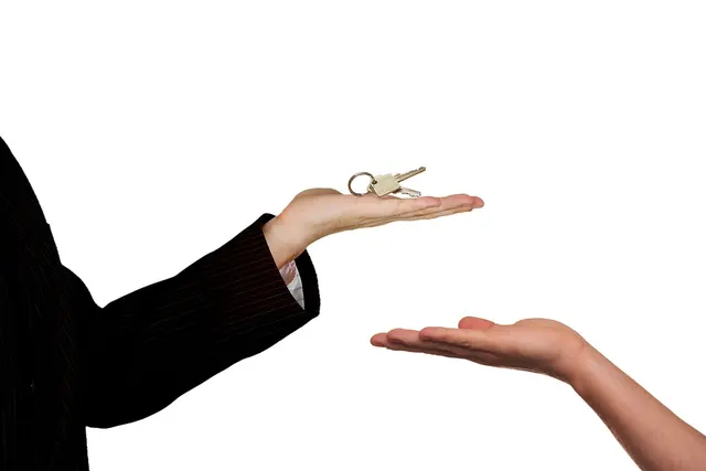 Hand in a dark pinstripe suit sleeve offering a set of keys above another person's open palm on a white background