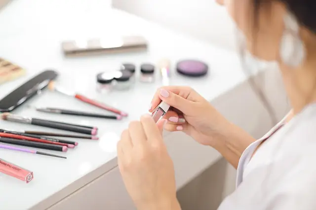 Woman arranging makeup brushes and lipsticks on a white counter