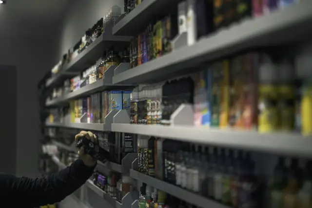 Hand reaching for products on a vape shop's packed shelves
